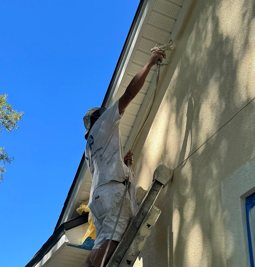 An A New Leaf painter on a ladder spraying the soffit line of a stucco home