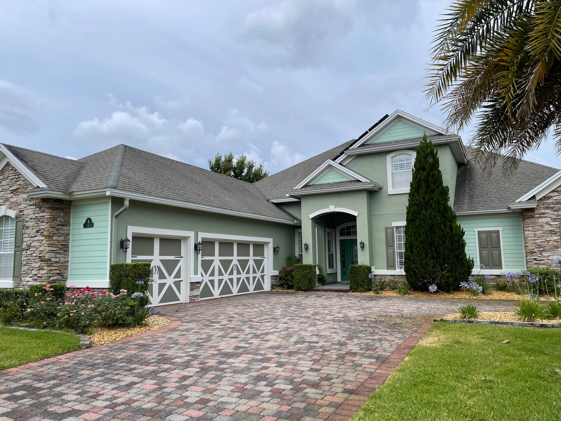 Sage green stucco home in Tidewater, Clapboard Creek, North Jacksonville FL 32226, after its exterior repaint, with white trim and carriage-style garage doors