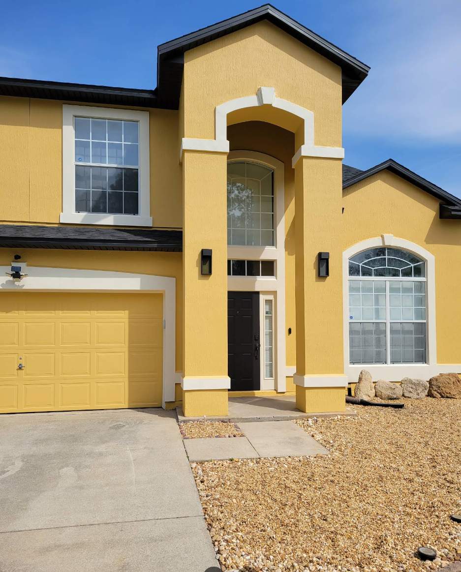 Two-story stucco home in Oakleaf Plantation, Orange Park FL after exterior painting, yellow with white trim