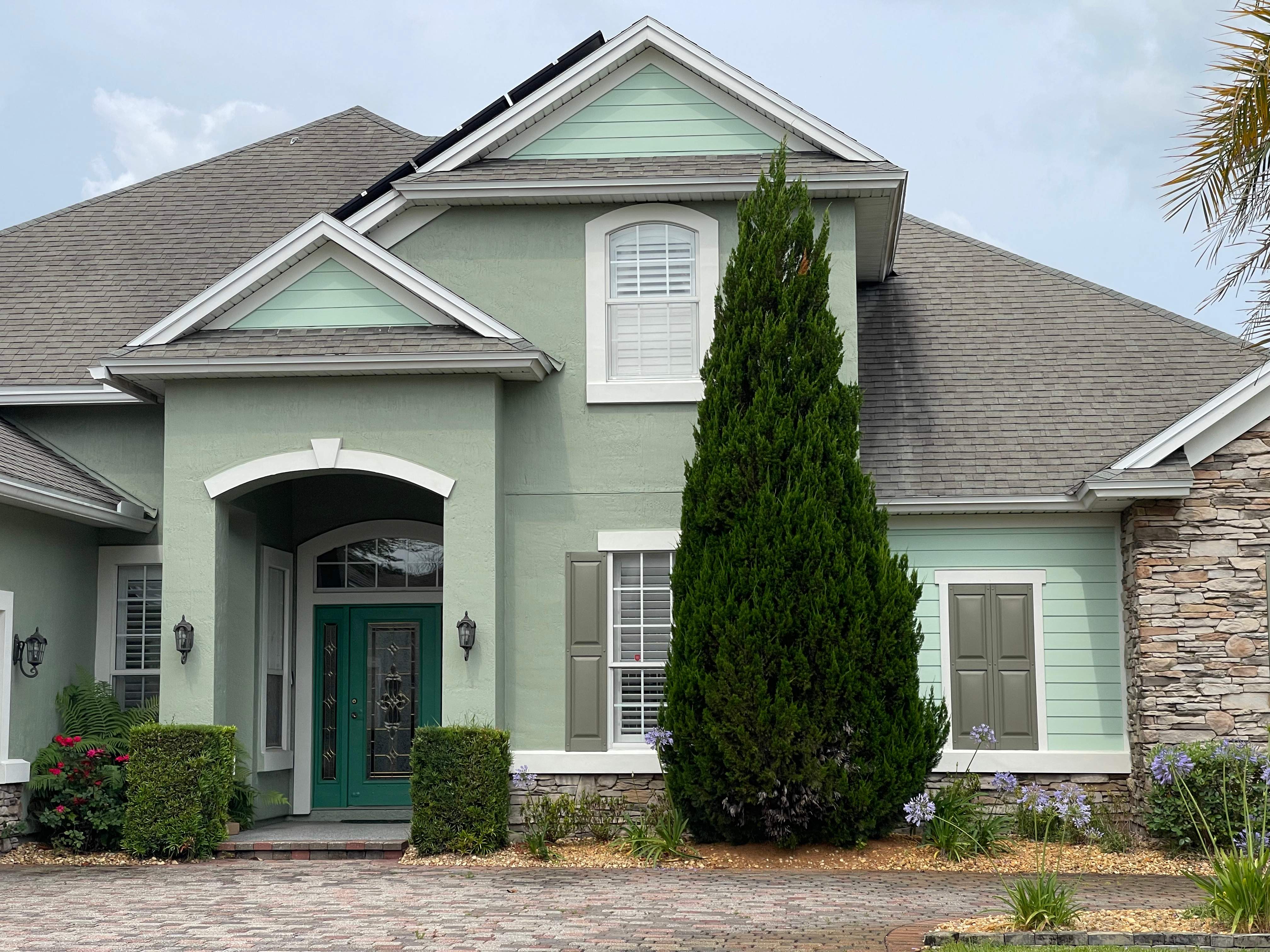 Entry of a Clapboard Creek home in North Jacksonville after exterior painting, with green stucco, a teal front door and painted shutters